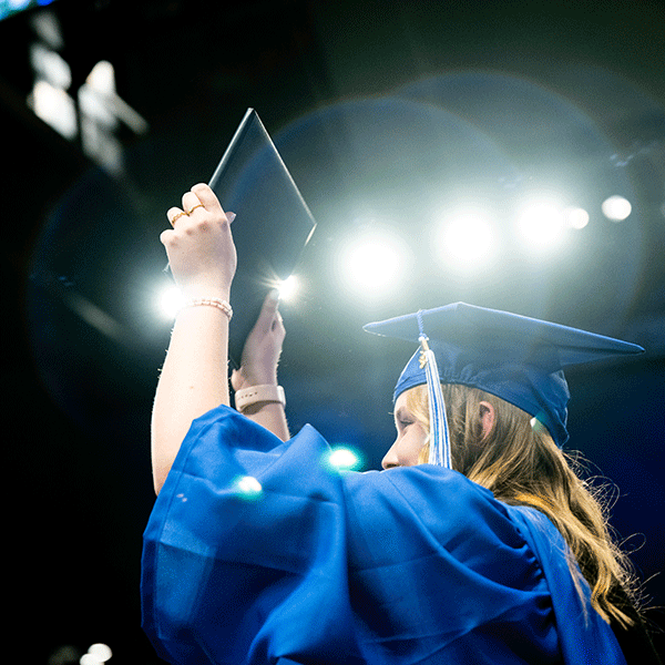 A student in a cap and gown holds up a diploma book